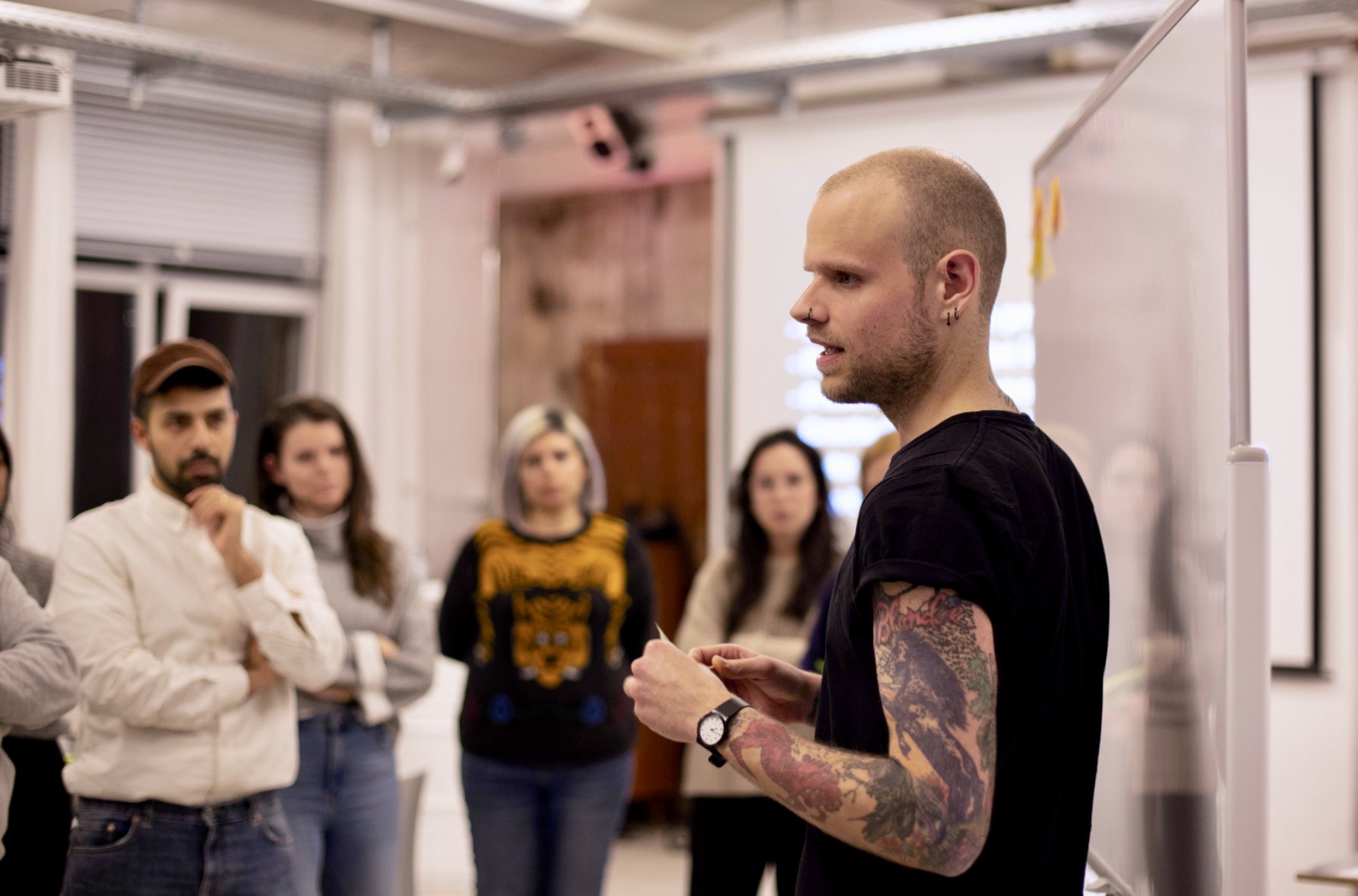 Daniel Majoros presenting to a small group of participants standing in front of a whiteboard in a studio space.